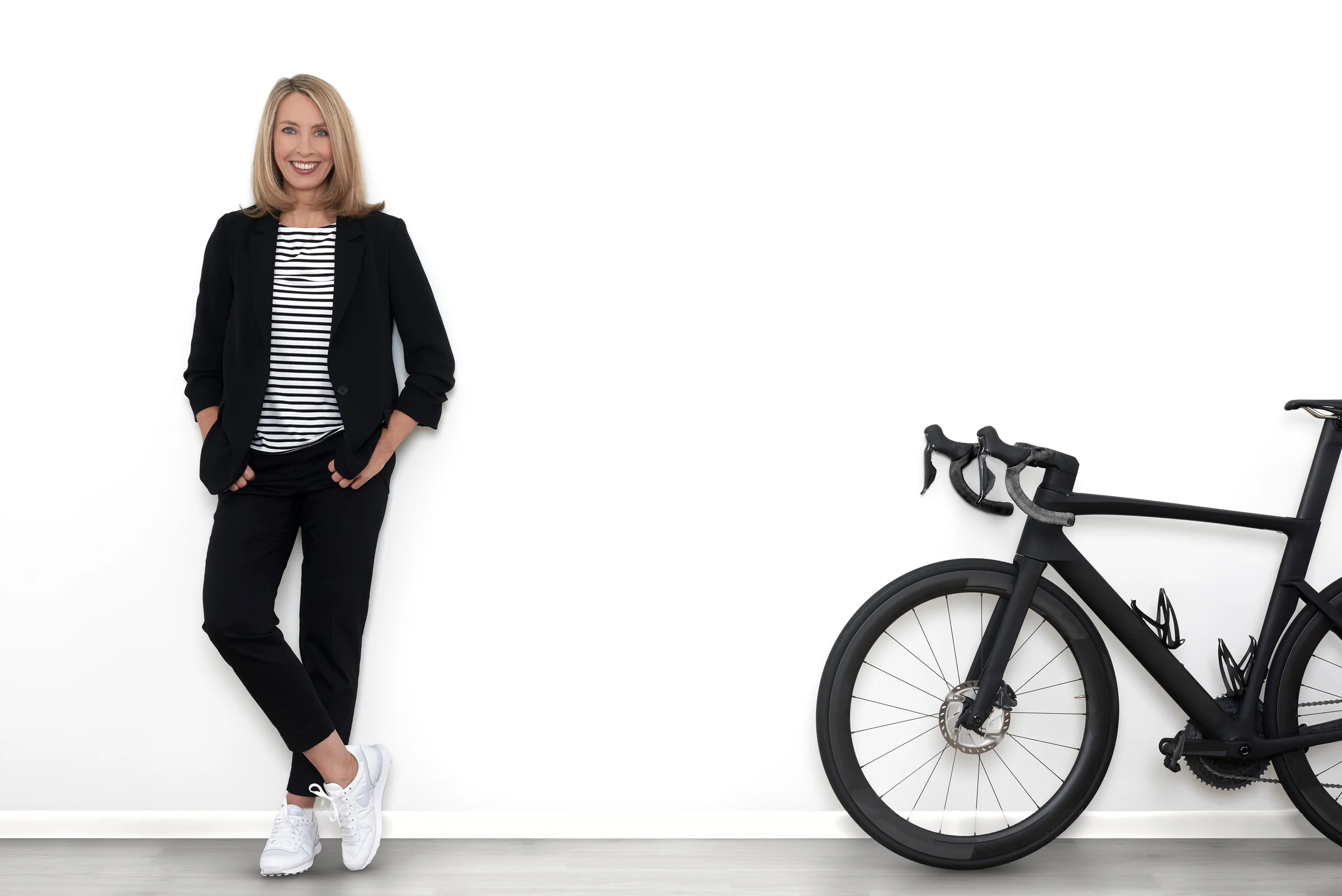 Sandra Kirstein lehnt an einer weissen Wand, daneben ihr schwarzes Rennrad